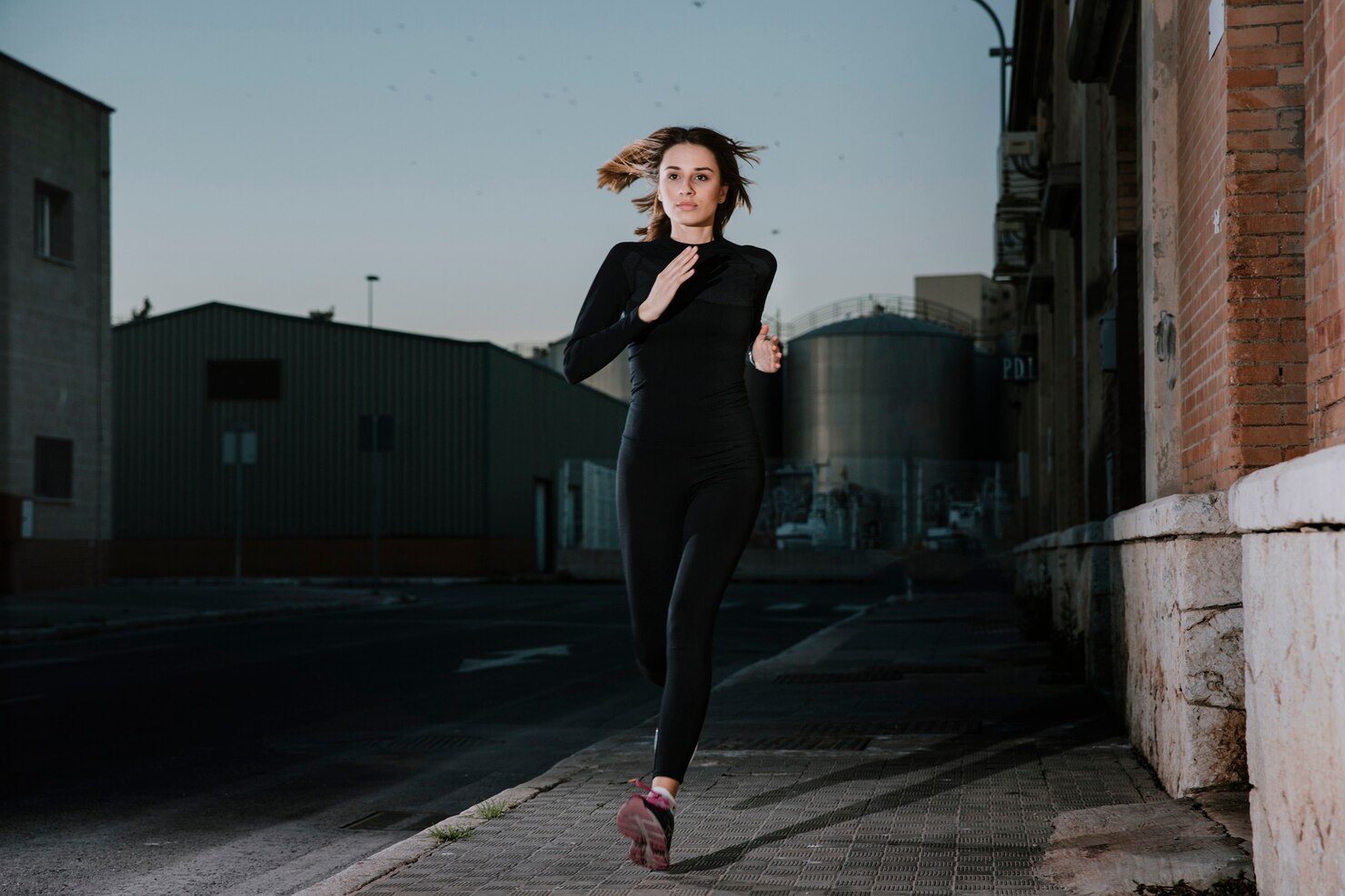 A focused runner trains on a quiet city street as daylight fades toward dusk.