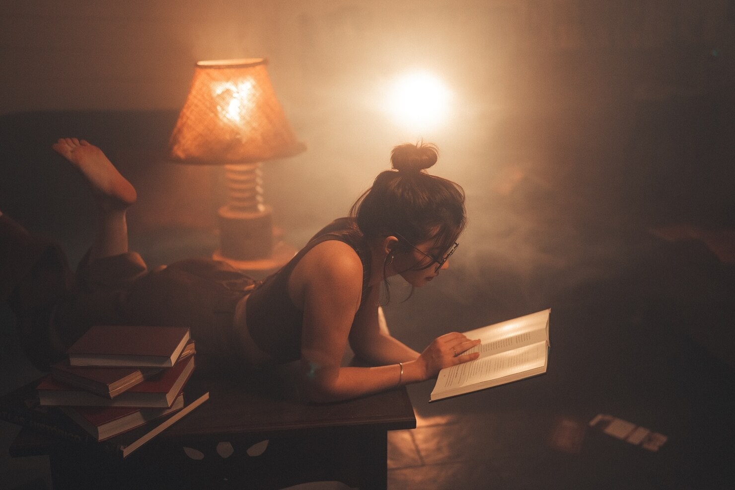 A woman lies on a sofa reading by warm lamps in an otherwise dark room.