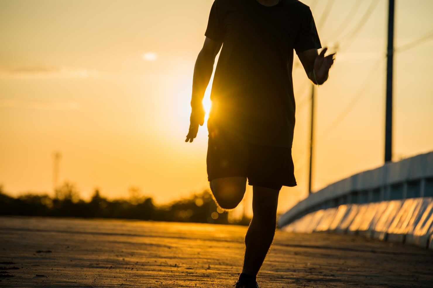 A runner moves along a bridge in warm low sunlight.