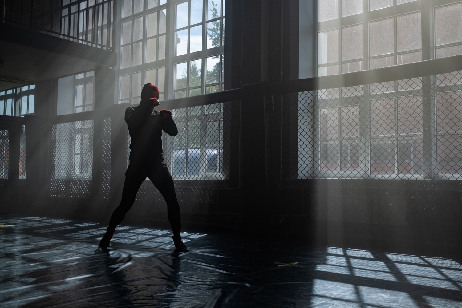 An athlete shadowboxes in a gym while strong daylight streams through tall windows.