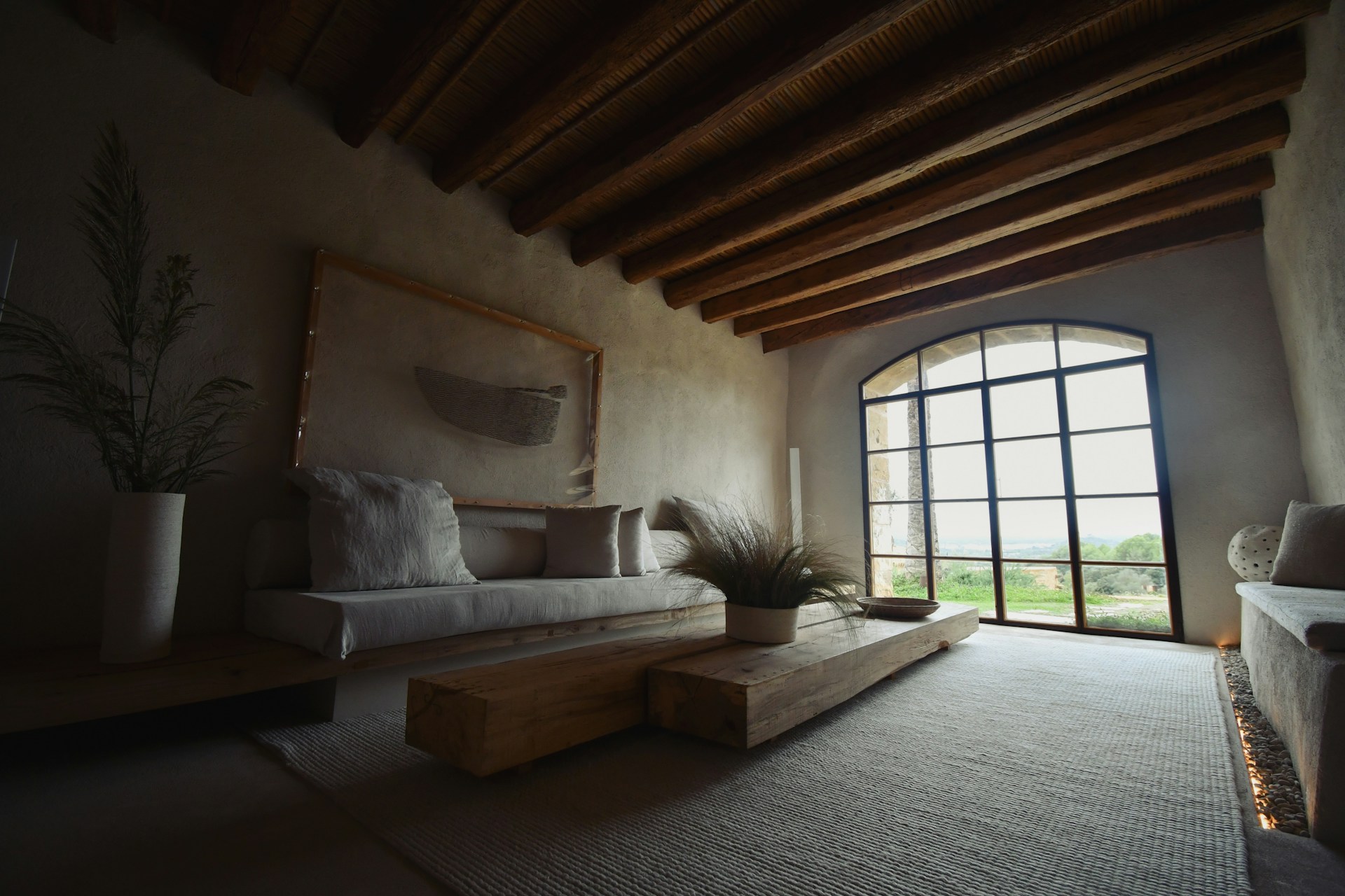 A person stands near a large window in a sunlit room, holding a cup and looking outside. The room is filled with natural morning light, featuring a potted plant and a cozy chair, creating a calm and refreshed atmosphere.