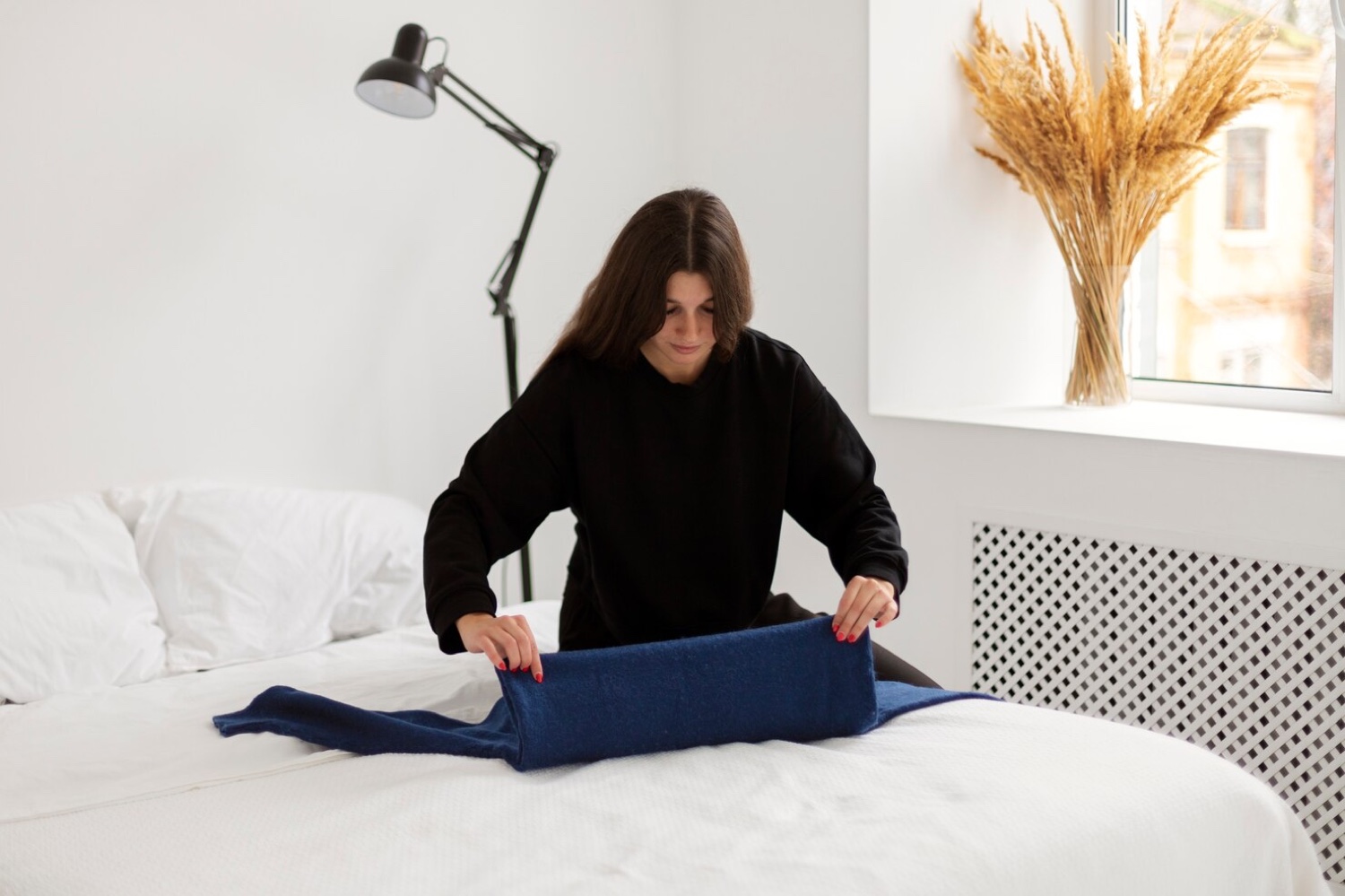 A woman folds clothes on her bed in daylight, preparing part of a future morning in advance.