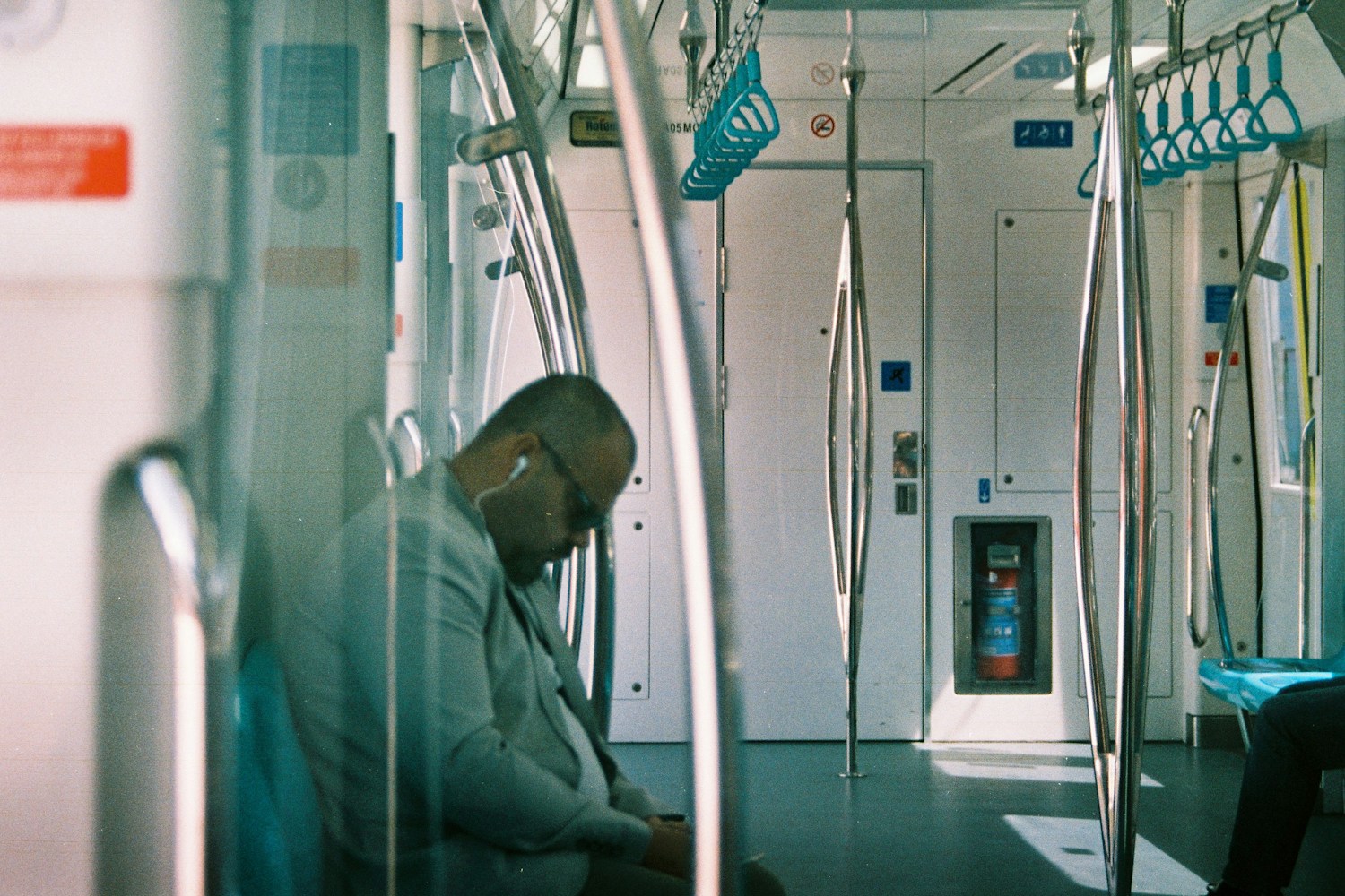 A commuter sleeps with earbuds in on a quiet morning train, illustrating the difficult mismatch between an early obligation and a body clock that has not caught up.