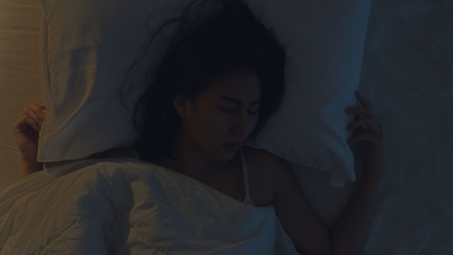 A person lies comfortably in bed, appearing peaceful and finally able to sleep well. Soft bedding and a dimly lit bedroom create a calm nighttime setting. The mood feels restful, relaxed, and reassuring.